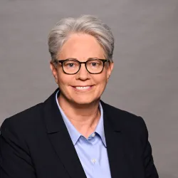 Portrait of a woman with short hair and glasses in a business suite with a blue shirt