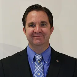 Photo of smiling man wearing a blue shirt, striped WVU tie and a dark suit jacket.